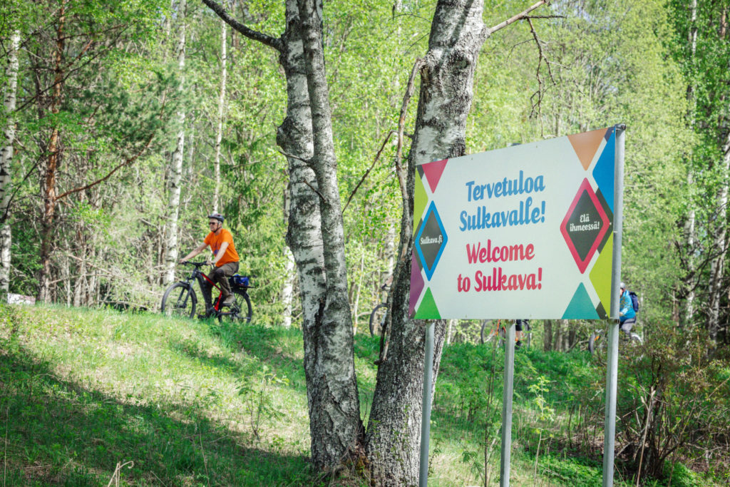 Pyöräilijät sillat - ja lossit pyöräilyreitillä "tervetuloa Sulkavalle" kyltin kanssa.