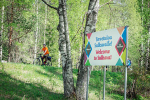 Pyöräilijät sillat - ja lossit pyöräilyreitillä "tervetuloa Sulkavalle" kyltin kanssa.